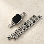 Silver cat Apple Watch band styled with jewelry in a light luxury flat lay